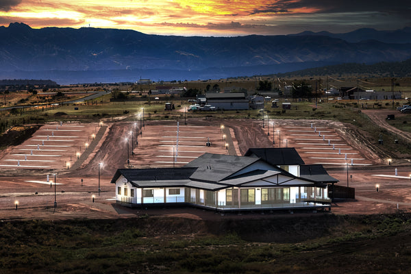 Dusk aerial of Observer Ranch: empty lit RV pads and the glowing Learning Center under a sunset sky in Penrose, Colorado