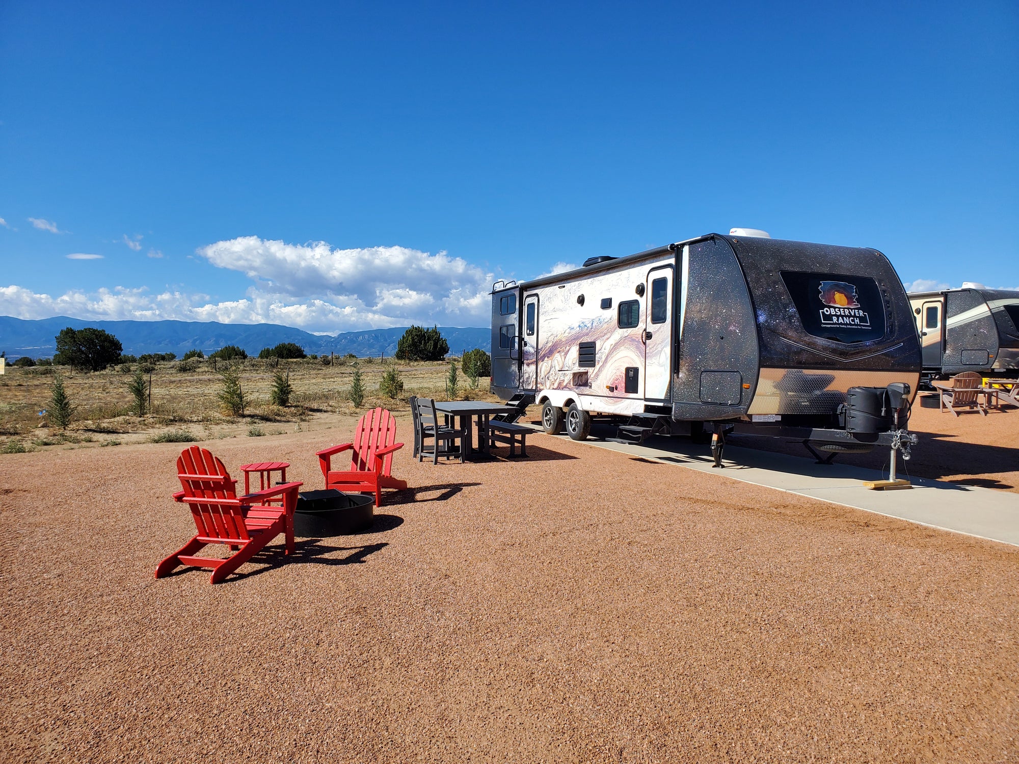 Jupiter planet camper wrap exterior with red Adirondack chairs and fire ring